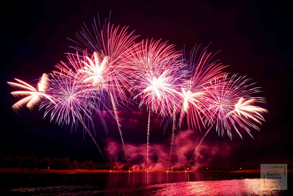 Red, pink and purple fireworks over lake at night