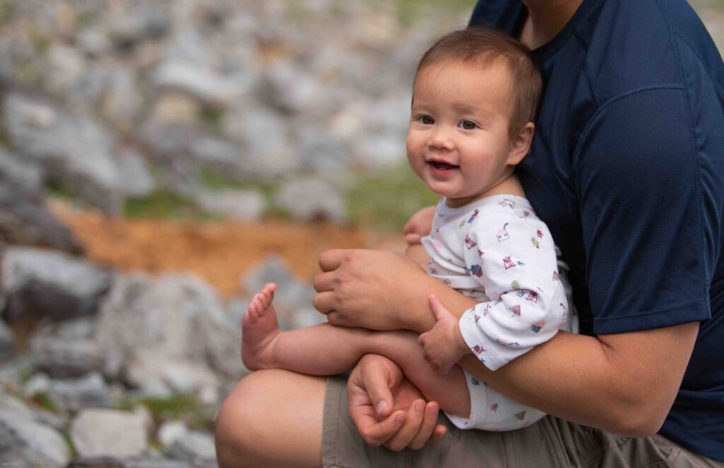 Baby sitting on father's lap in nature